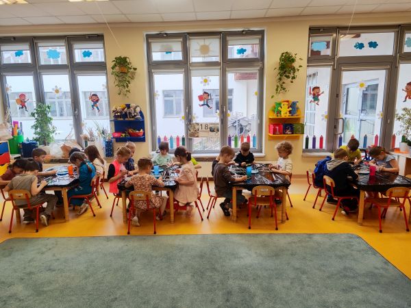 zdjęcie przedszkolaków siedzących przy stolikach podczas zajęć